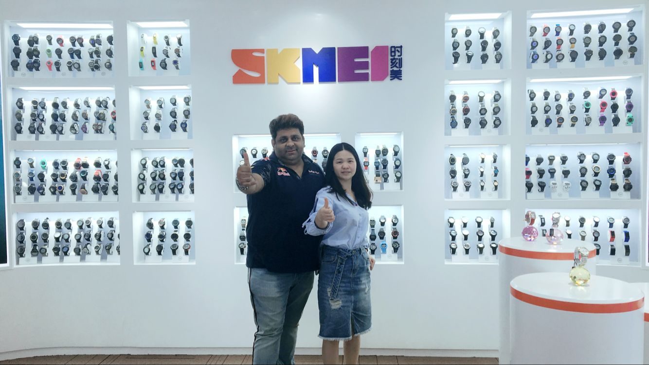 Overseas customer and SKMEI representative giving thumbs up in front of the sample wall, May 2019